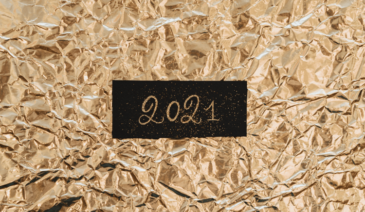Zdjęcie tabliczki z napisem "2021" na tle pomarszczonego złotego papieru