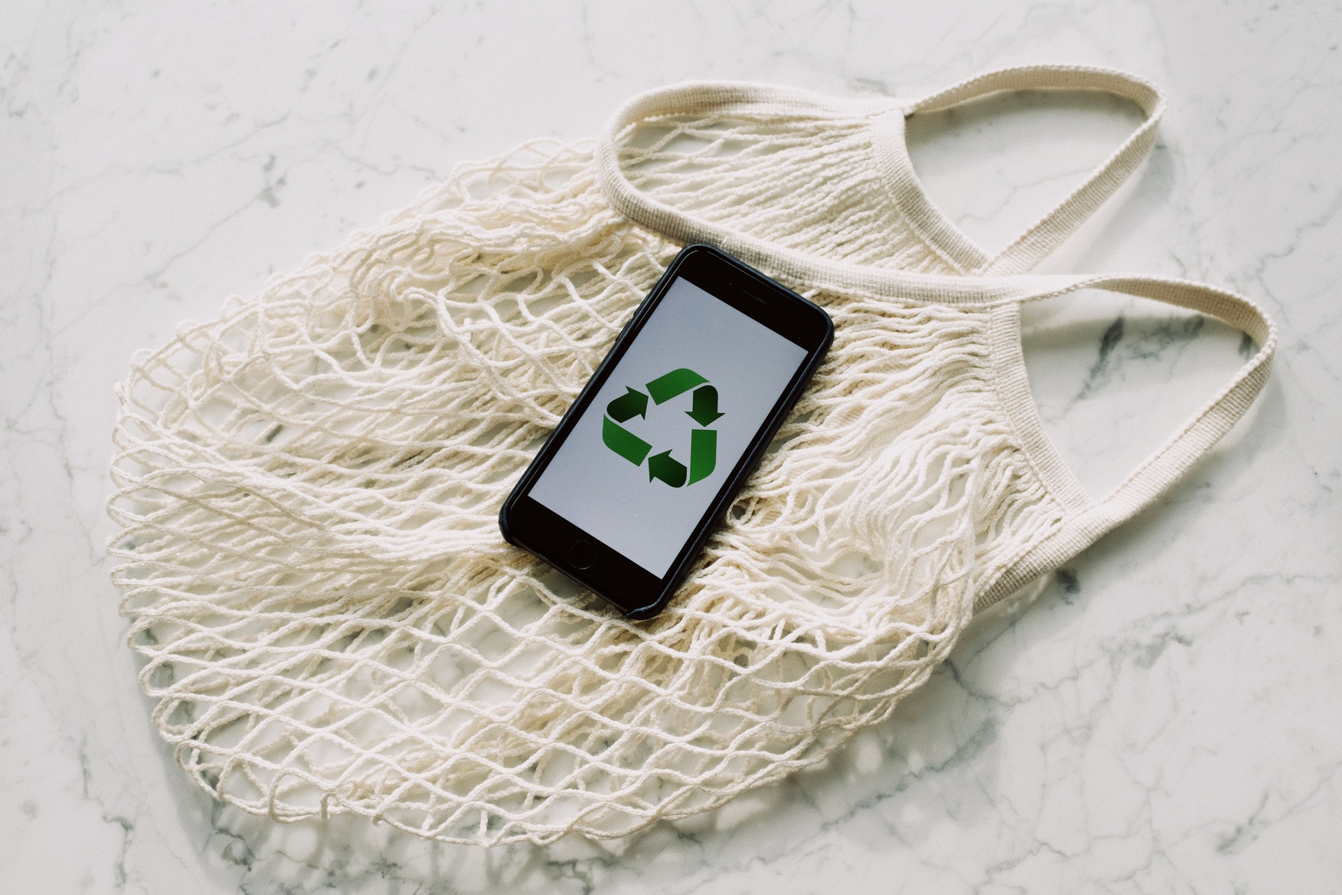 Zdjęcie wielorazowej siatki i leżącego na niej telefonu z symbolem recyklingu na ekranie