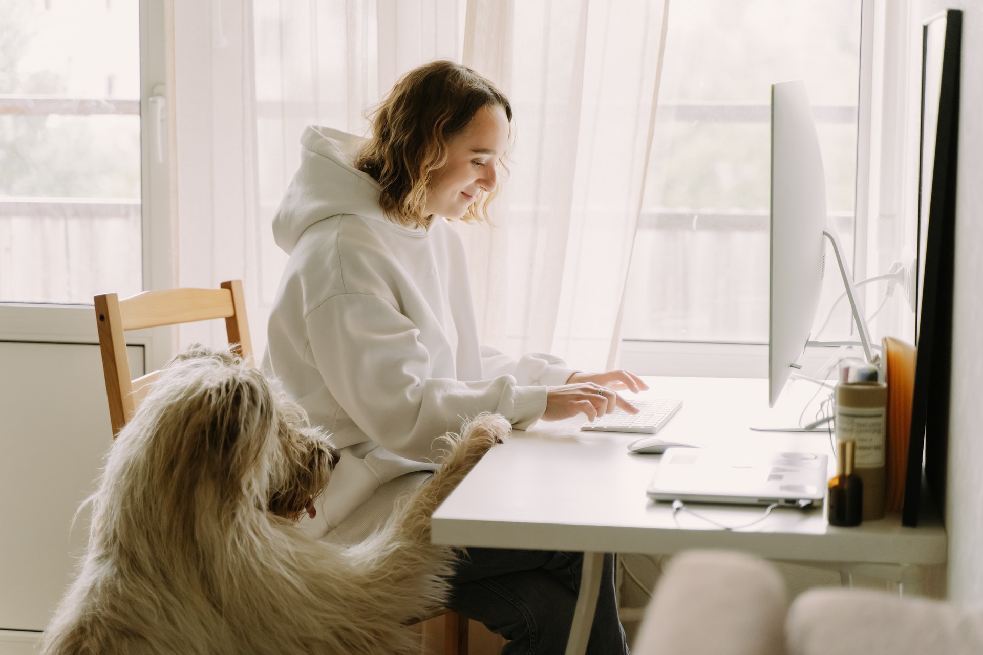 Zdjęcie kobiety przed komputerem oraz jej psa, który kładzie łapkę na biurku