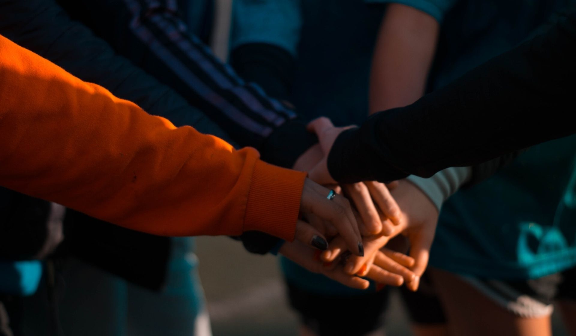 A photo of five people's hands, clasped together